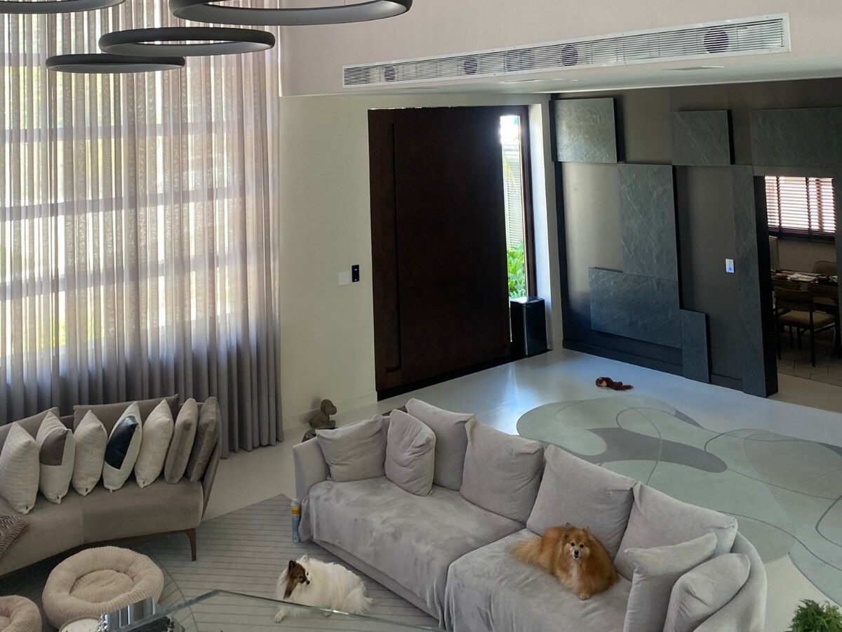 Sala de estar com grelha linear de ar-condicionado embutida no rebaixo sobre o vão de passagem, com dois cães no sofá