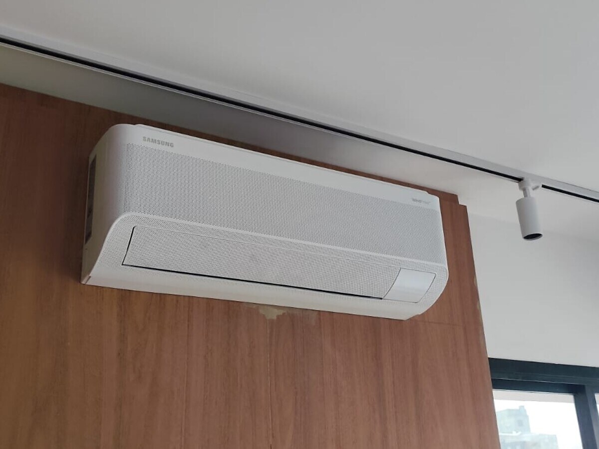 Evaporadora de ar-condicionado instalada sobre painel de madeira em ambiente com pé-direito alto e janela