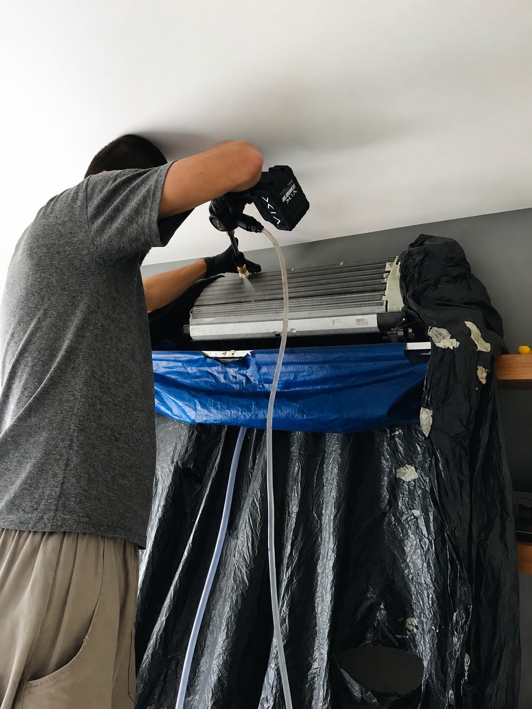Técnico lavando a serpentina de uma evaporadora hi-wall com equipamento de pressão, com o ambiente protegido por lonas