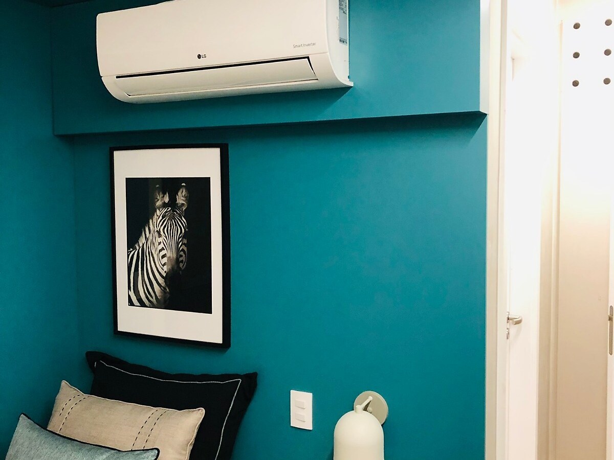 Evaporadora de ar-condicionado instalada no alto da parede de um quarto com paredes azul-petróleo